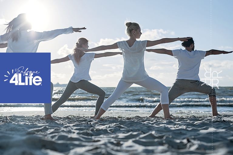 Cuatro personas haciendo yoga en una playa soleada, rejuveneciendo cuerpo y mente junto al mar.
