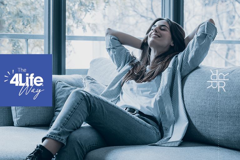 Woman sitting on a couch, smiling with her hands behind her head enjoying living the 4Life way