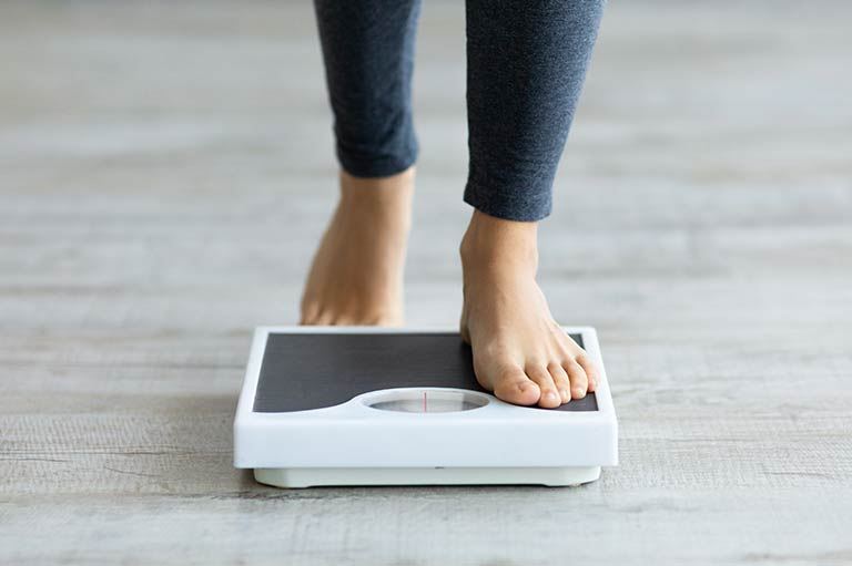 Close-up of person's feet standing on a scale, highlighting GLP-1's support in weight management.