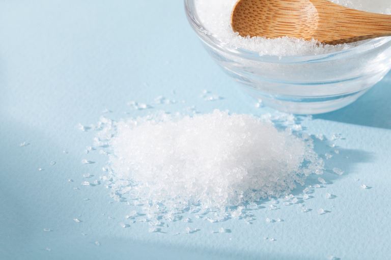 White magnesium salt next to a glass bowl filled with more salt, with a wooden spoon resting on top.