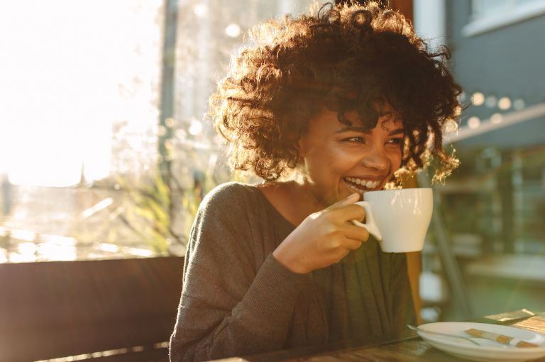 a smiling girl holding a white cup of coffee