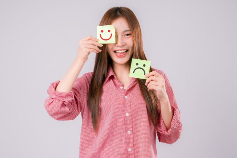 a smiling woman with a card with a smile painted and another card with a sad face painted
